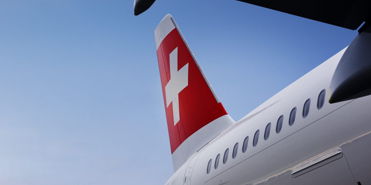 SWISS plane tail, iconic red and white cross under a blue sky.
