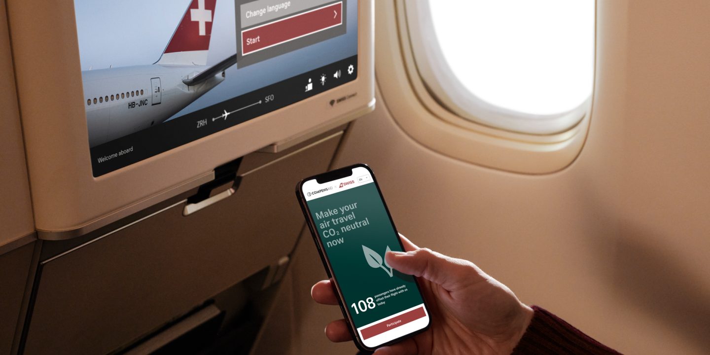 Passenger uses phone app for CO2 offsetting on a SWISS flight. In-flight screen shows plane tail.