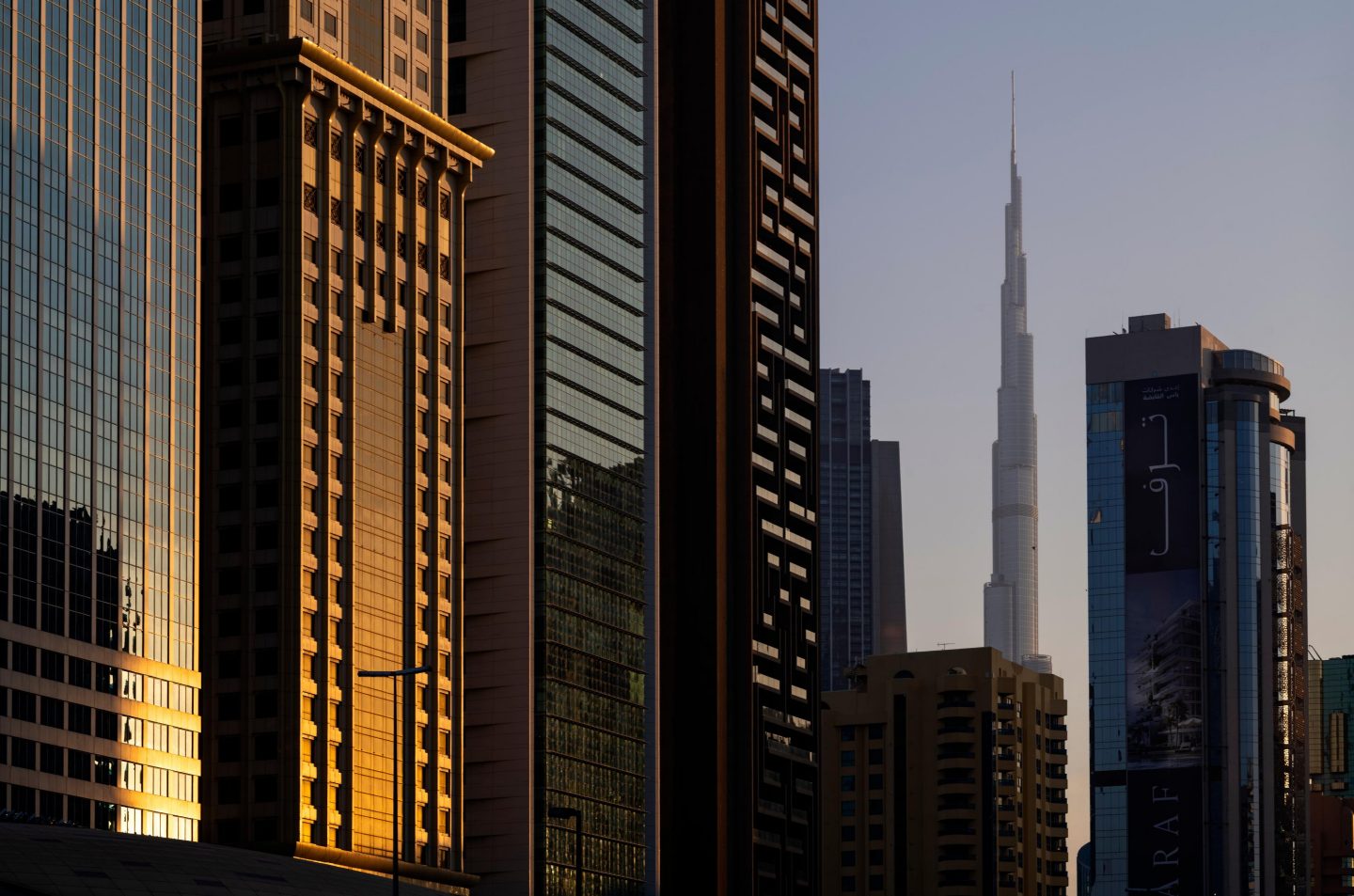 Dubai skyline with the Burj Khalifa rising between modern skyscrapers at sunset.