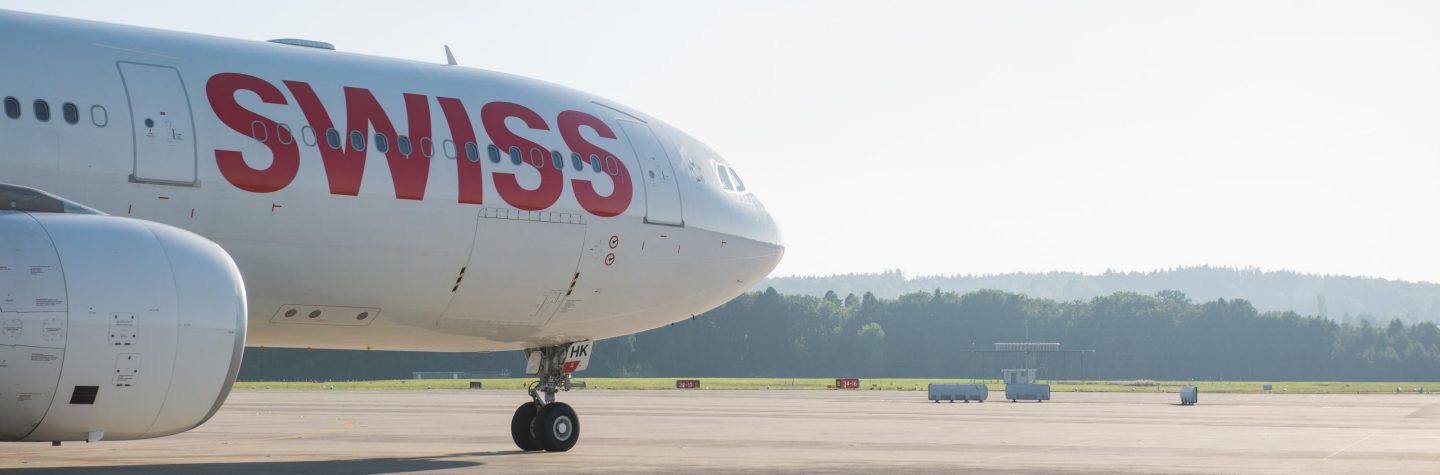 Swiss aircraft on sunny tarmac between trees.