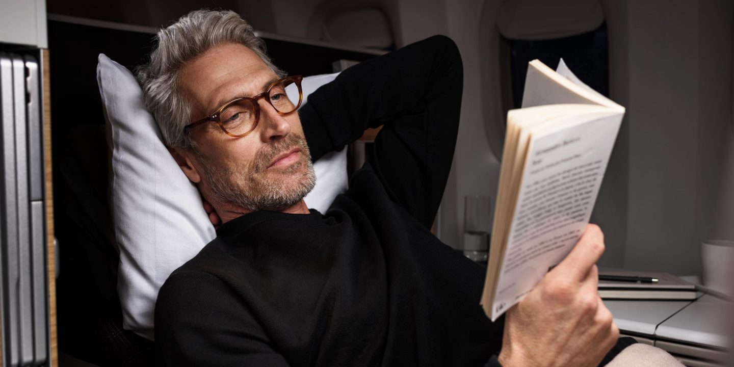 A man reads a book in an aeroplane seat.