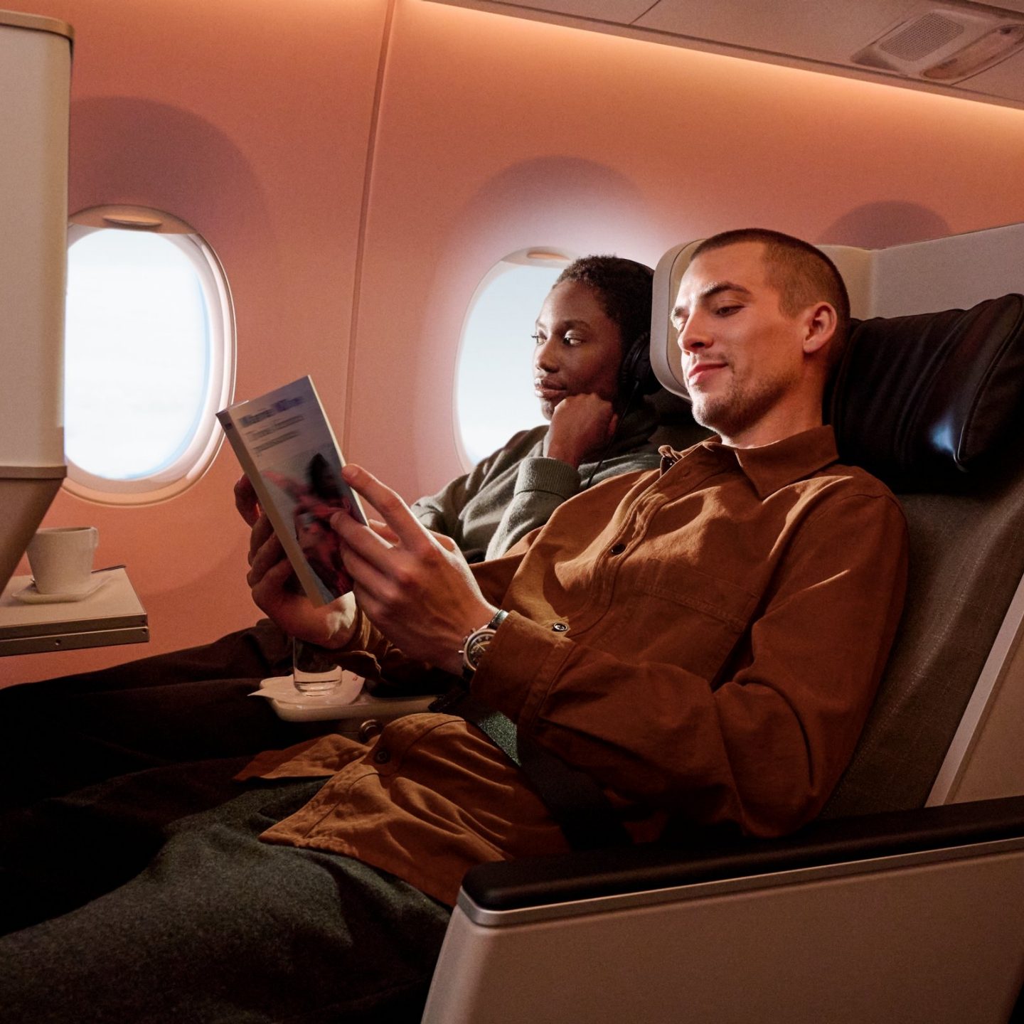 A couple relaxing and reading in the comfortable seats of a modern SWISS First Class cabin.