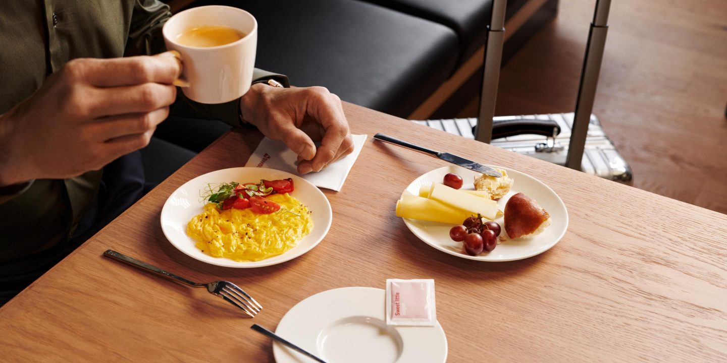 A man seated at a table, eating breakfast surrounded by plates of food and meal vouchers.