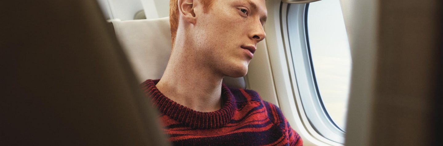 Red-haired passenger holding a smartphone and looking out the window in a SWISS airplane cabin.