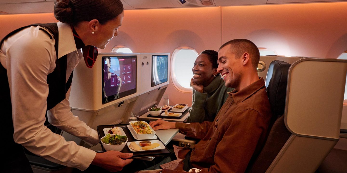 Flight attendant serves delicious meals to smiling passengers enjoying their premium cabin.