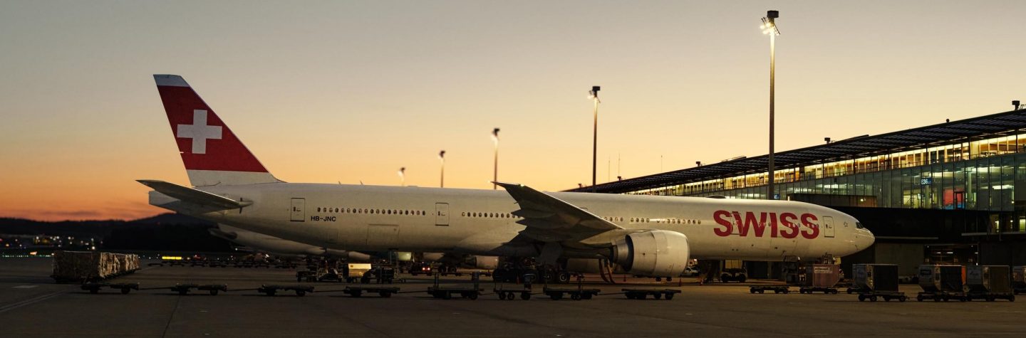 A SWISS Boeing 777-300ER parked at an airport terminal at dusk.