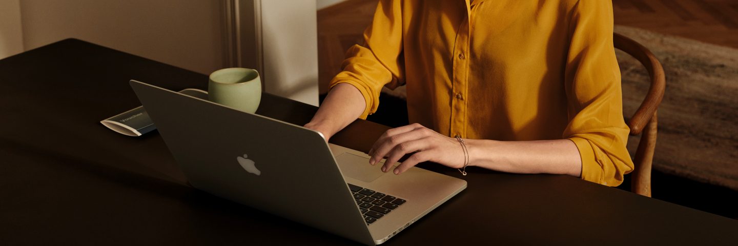 A woman seated at a table, typing on her laptop, engaged in her tasks.