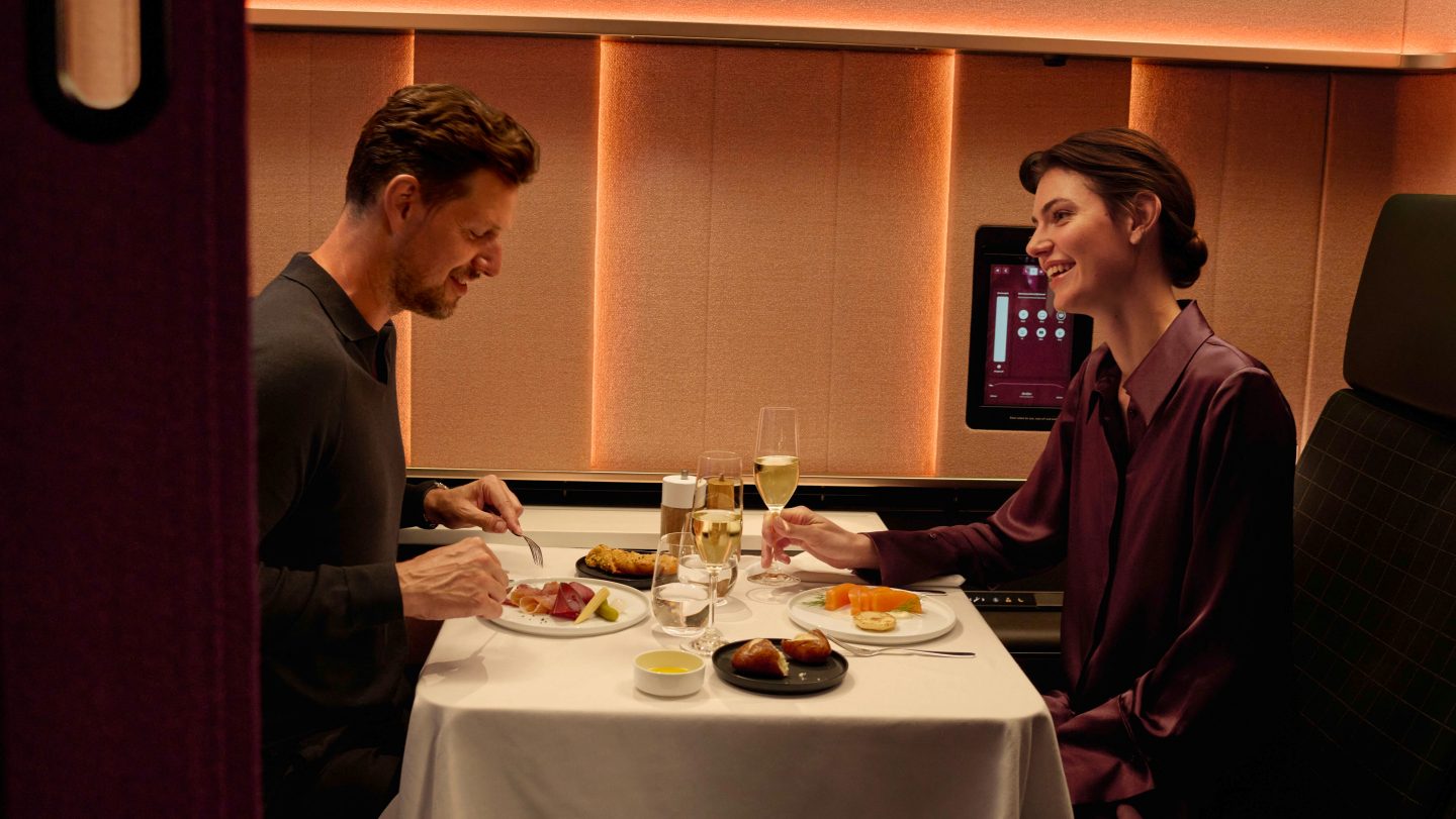 Smiling couple enjoys a private meal with champagne in a premium airline cabin.
