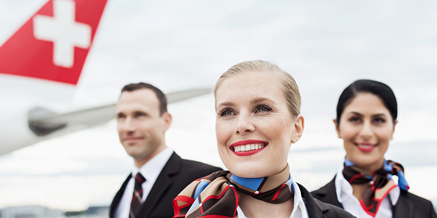 Friendly flight crew smiling in uniform with a Swiss airplane tail.