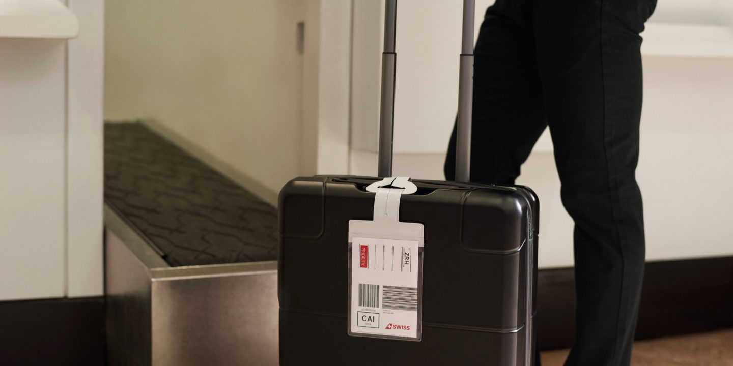 Individual next to a suitcase displaying a home-printed baggage tag.