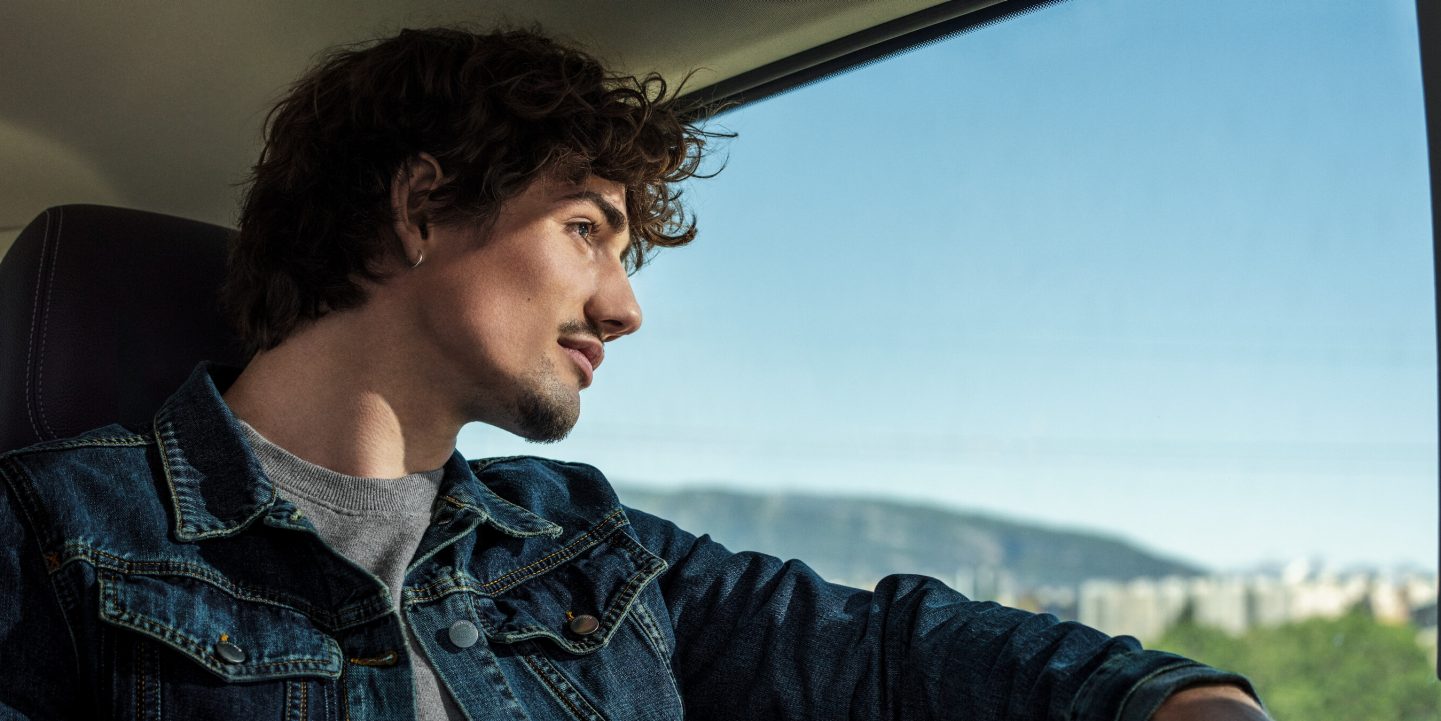 Man looking out window at a bright blue sky, anticipating travel.