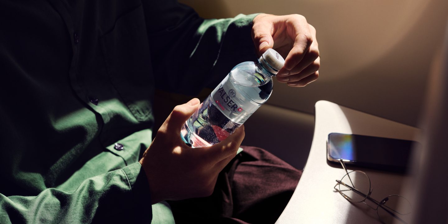 A person holding a bottle of Valser mineral water on a plane.