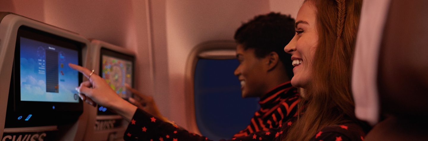 Two smiling women enjoying the inflight entertainment system on a SWISS flight.