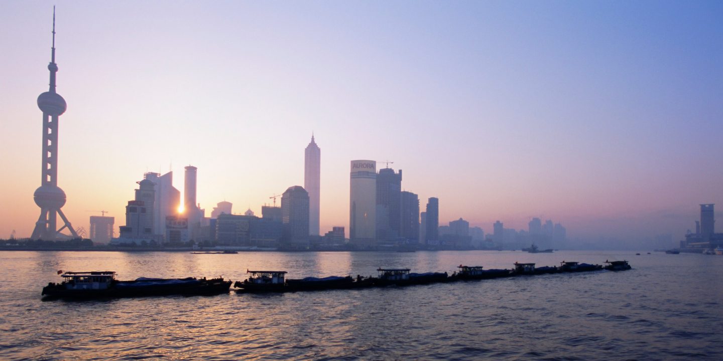 The Shanghai skyline at sunrise, featuring towering skyscrapers bathed in warm, golden light.