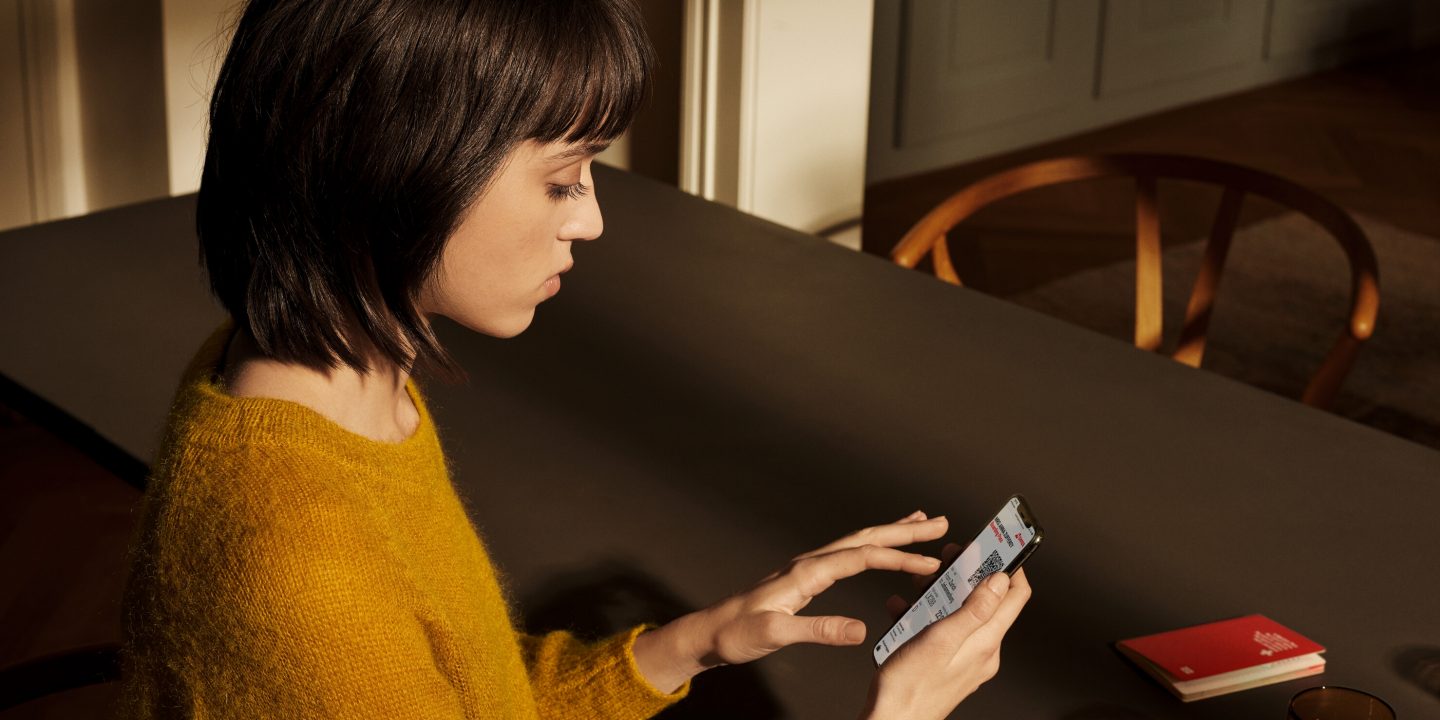 A woman seated at a table, using a phone while a book lies open beside her.