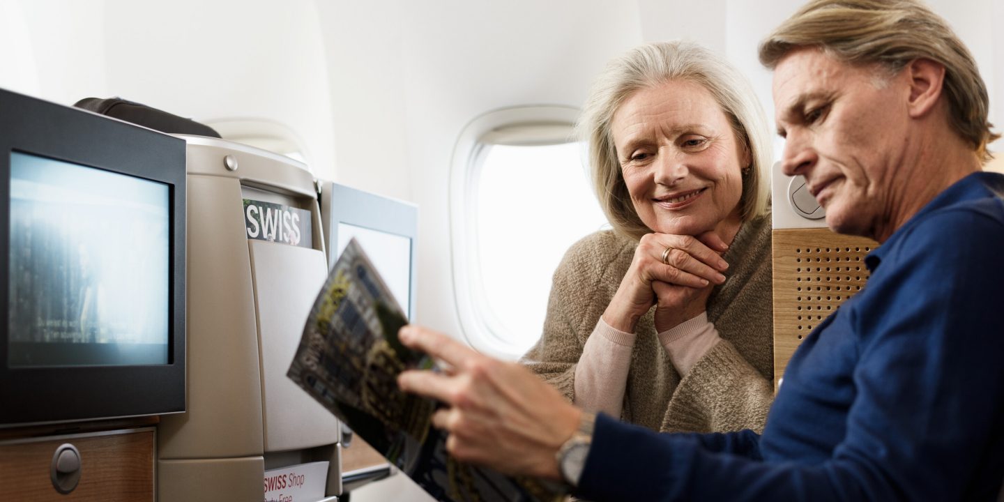 Couple smiles while reading a SWISS magazine in comfort on their flight.