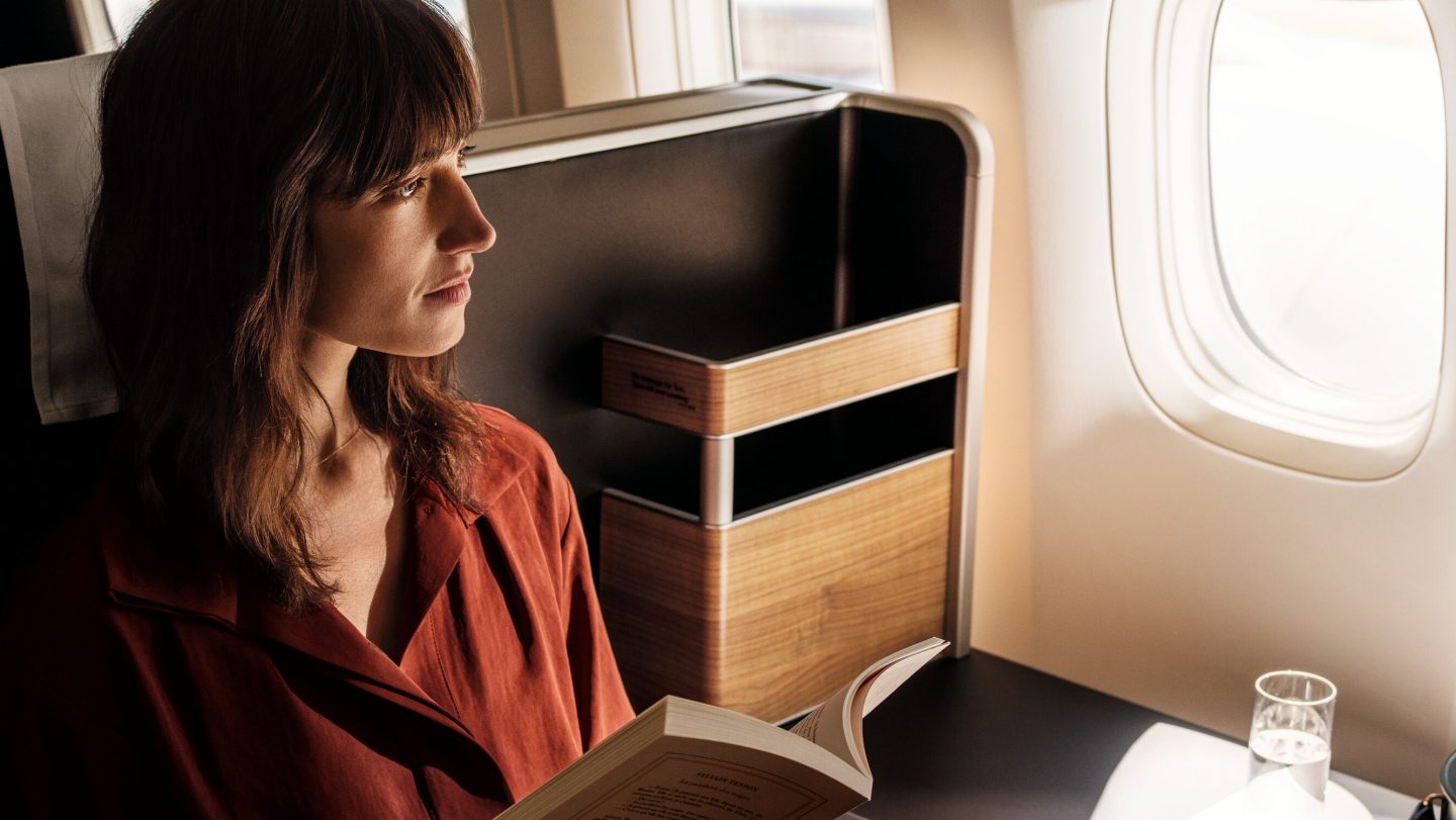 Woman reading a book, gazing out the window from her spacious airline seat.