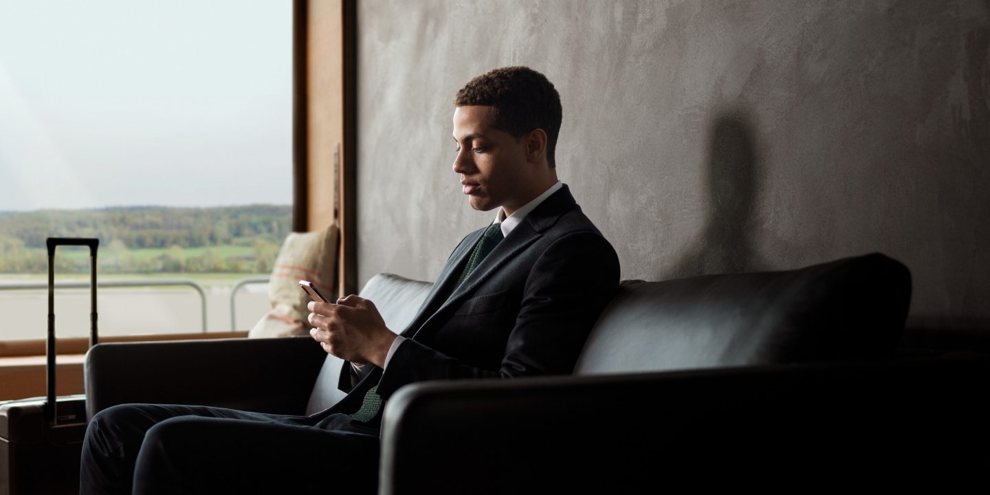Business traveler using phone in a sleek airport lounge, suitcase waiting.