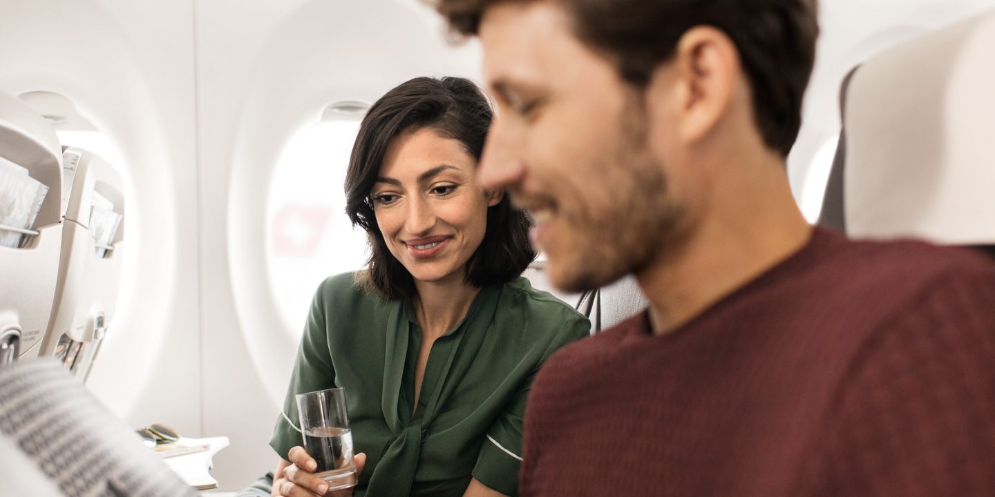 Smiling woman with a drink, enjoying a bright airline flight.