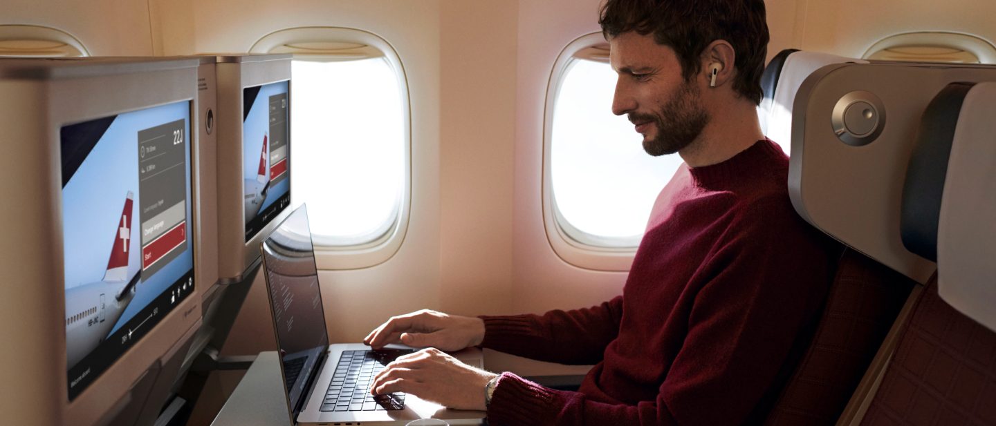 Junger Mann hält ein Smartphone. Er nutzt das Internet an Bord, um online Musik zu hören.