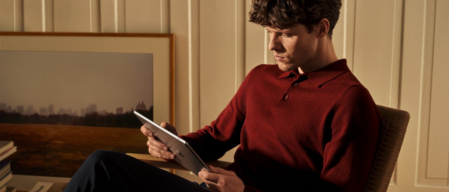 Junger Mann sitzt in einem Sessel und nutzt ein Tablet.